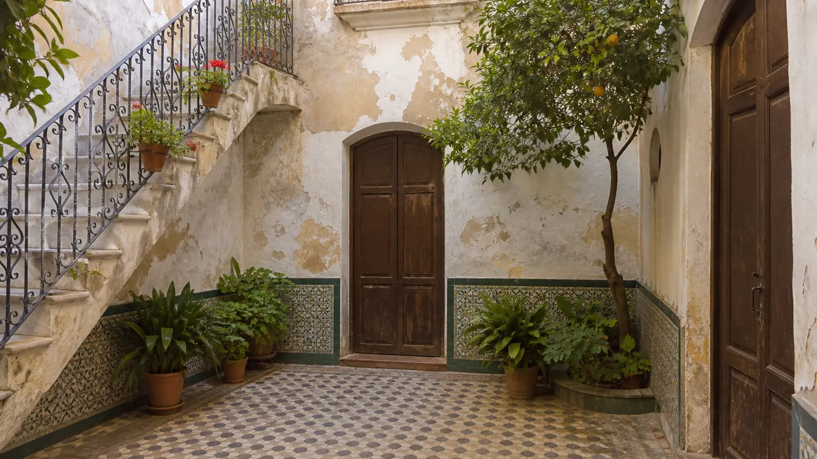 Andalusian patio with old tiles, an iron staircase and pots of geraniums
