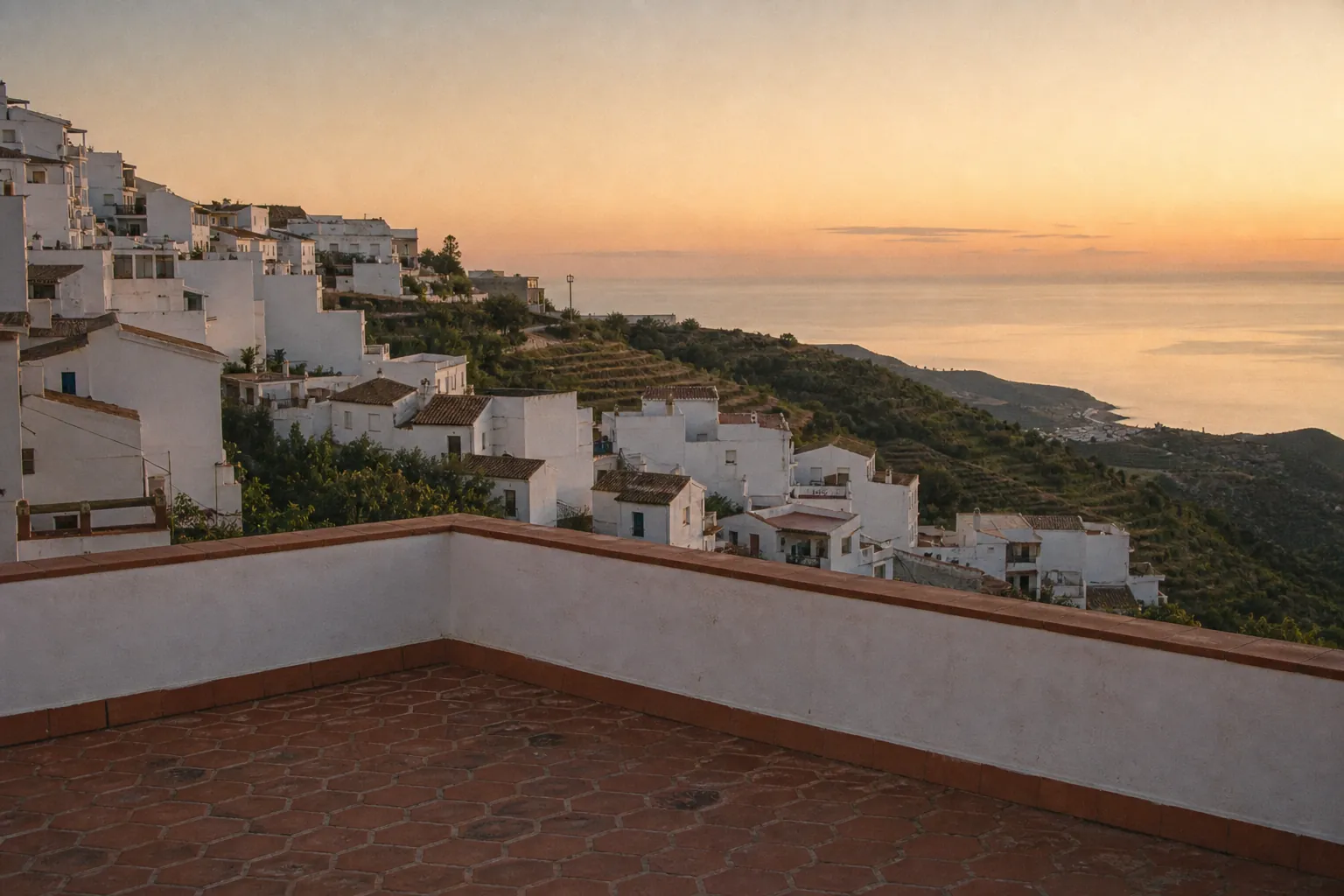 Pueblo blanco de la Axarquía escalonado hacia el mar al atardecer, visto desde una terraza vacía