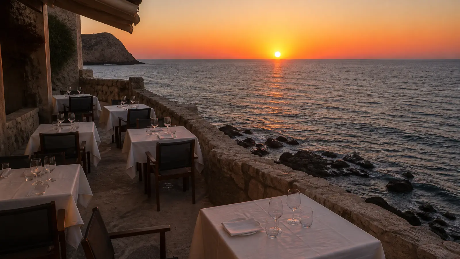 The restaurant terrace on the rocks at sunset, white tablecloths and the sea behind